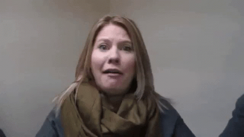 A Woman Wearing A Scarf And A Sweater Is Standing In Front Of A Wall With Her Arms Outstretched . GIF