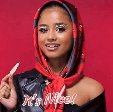 A Woman Wearing A Scarf Around Her Head Is Holding A Piece Of Food And Says It 'S Nice GIF
