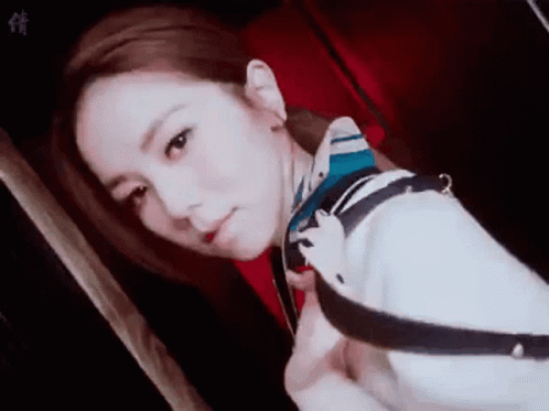 A Woman Wearing A Scarf Around Her Neck Is Taking A Selfie In A Dark Room . GIF