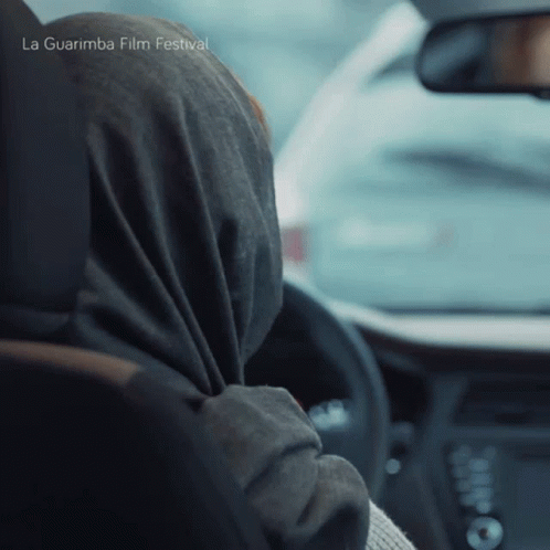 A Woman Wearing A Scarf Is Driving A Car With La Guarimba Film Festival Written On The Bottom Of The Image GIF