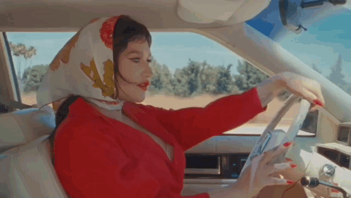 A Woman Wearing A Scarf Is Driving A Car . GIF