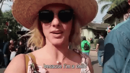 A Woman Wearing A Straw Hat And Sunglasses Is Standing In A Crowded Area . GIF