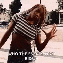 A Woman Wearing A Striped Crop Top And Shorts Is Standing On A Sidewalk . GIF