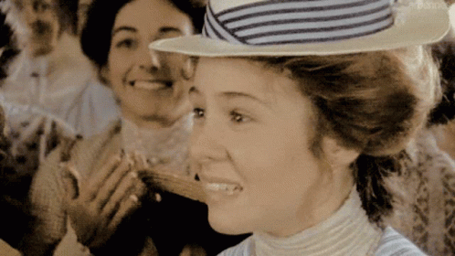 A Woman Wearing A Striped Hat Is Smiling In Front Of Two Other Women GIF