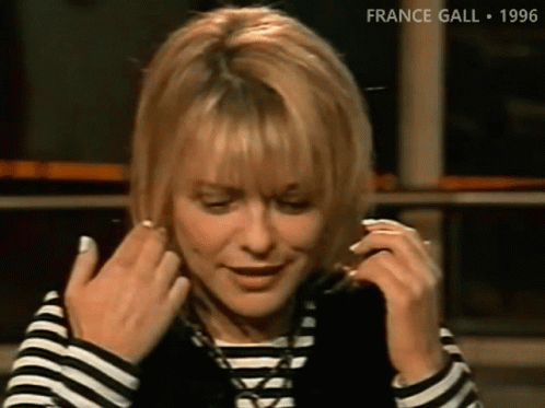 A Woman Wearing A Striped Shirt And A Black Vest Adjusts Her Hair GIF