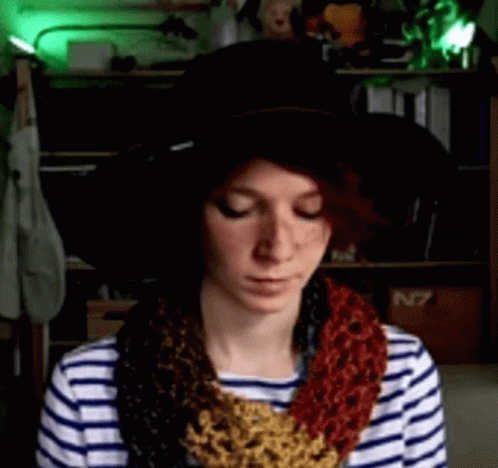 A Woman Wearing A Striped Shirt And A Hat With A Scarf Around Her Neck Is Looking Down GIF
