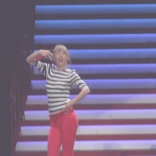 A Woman Wearing A Striped Shirt And Red Pants Is Dancing On A Stage GIF