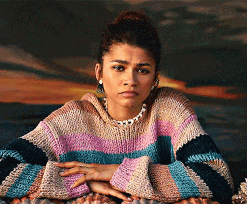 A Woman Wearing A Striped Sweater And A Pearl Necklace Looks At The Camera GIF