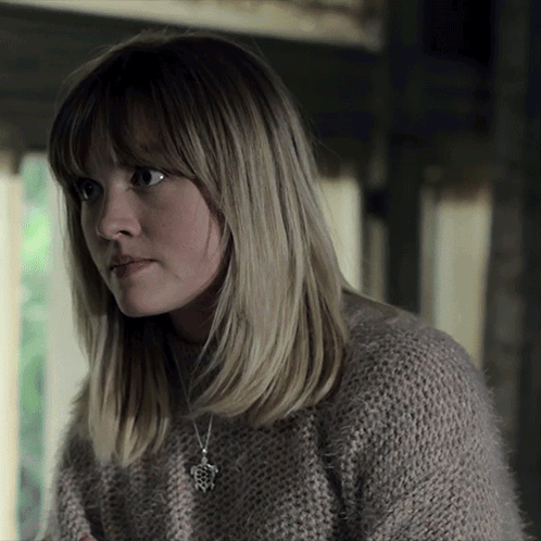 A Woman Wearing A Sweater And A Necklace With A Pendant That Looks Like A Frog GIF