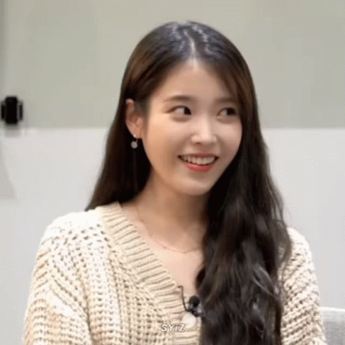 A Woman Wearing A Sweater And Earrings Is Smiling And Looking At The Camera . GIF