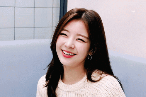 A Woman Wearing A Sweater And Hoop Earrings Smiles For The Camera GIF