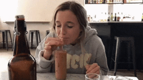 A Woman Wearing A Sweatshirt That Says Acdc Drinks From A Bottle GIF
