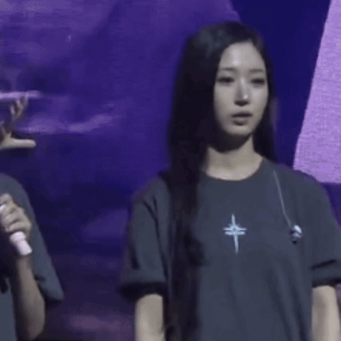 A Woman Wearing A T-Shirt With A Cross On It Is Waving Her Hand GIF