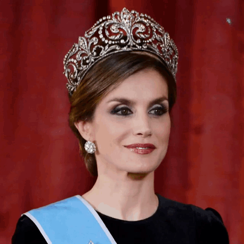 A Woman Wearing A Tiara And A Blue Sash Looks At The Camera GIF
