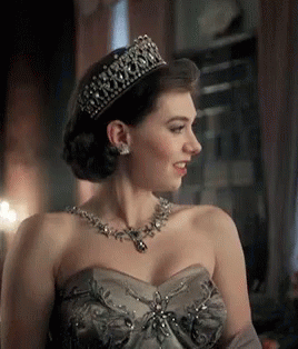 A Woman Wearing A Tiara And A Necklace Is Smiling . GIF