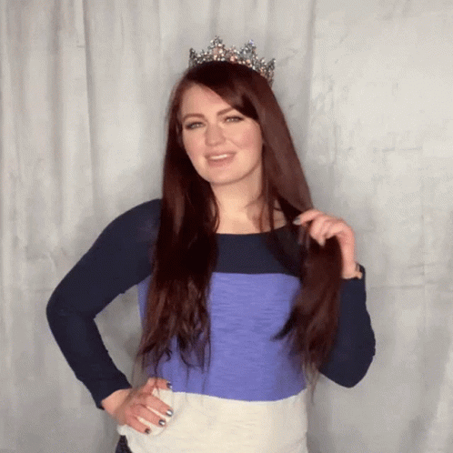 A Woman Wearing A Tiara And A Striped Shirt Holds Her Hair GIF