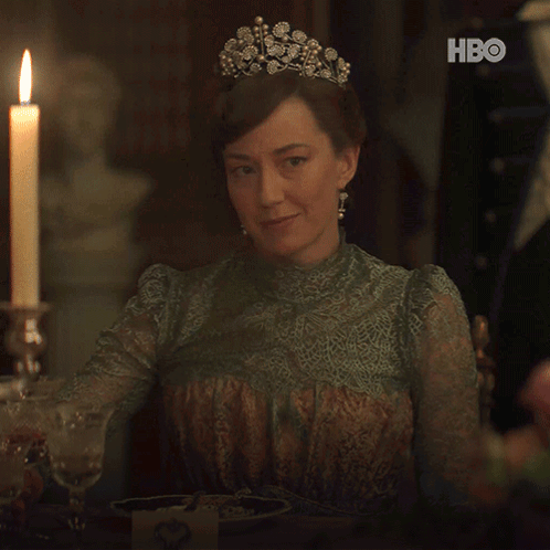 A Woman Wearing A Tiara Is Holding A Glass Of Wine In Front Of A Candle And Hbo Logo GIF