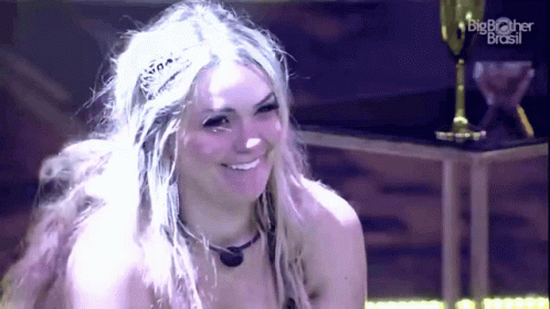 A Woman Wearing A Tiara Is Smiling In Front Of A Big Brother Brasil Logo GIF
