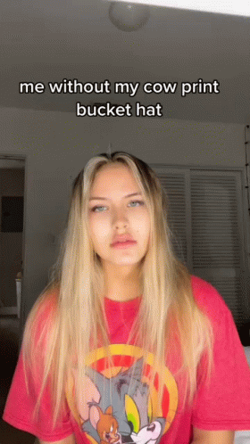 A Woman Wearing A Tom And Jerry Shirt Says " Me Without My Cow Print Bucket Hat " On The Bottom GIF