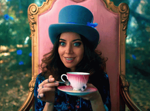A Woman Wearing A Top Hat Is Sitting In A Chair Drinking From A Teacup GIF