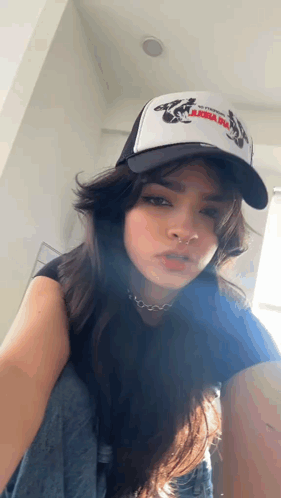 A Woman Wearing A Trucker Hat And A Nose Ring Is Kneeling Down . GIF