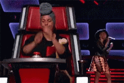 A Woman Wearing A Turban Is Sitting In A Chair On A Stage With A Microphone . GIF