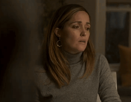 A Woman Wearing A Turtleneck Sweater And Earrings Is Sitting At A Table With Her Mouth Open . GIF