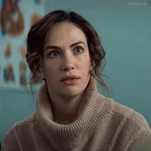 A Woman Wearing A Turtleneck Sweater Is Looking At The Camera . GIF