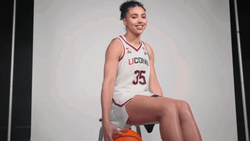 A Woman Wearing A Uconn Jersey Sits On A Stool With A Basketball GIF