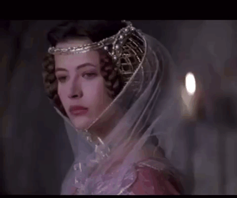 A Woman Wearing A Veil And A Crown Looks At The Camera GIF