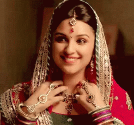 A Woman Wearing A Veil And Jewelry Is Smiling And Looking At Her Necklace . GIF