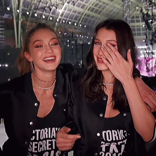 A Woman Wearing A Victoria 'S Secret Shirt Laughs With Another Woman GIF