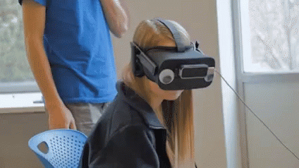 a woman wearing a virtual reality headset is sitting in a chair next to a man in a blue shirt .