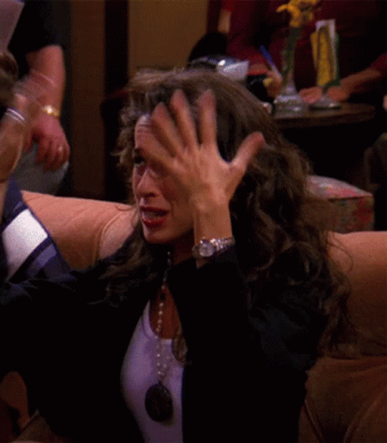 A Woman Wearing A Watch Is Sitting On A Couch Covering Her Face With Her Hand GIF