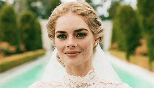 A Woman Wearing A Wedding Dress And Veil Smiles For The Camera GIF
