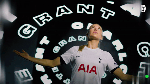 a woman wearing a white aia jersey stands in front of a circle of letters