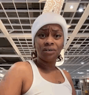 a woman wearing a white beanie and a white tank top is making a funny face .