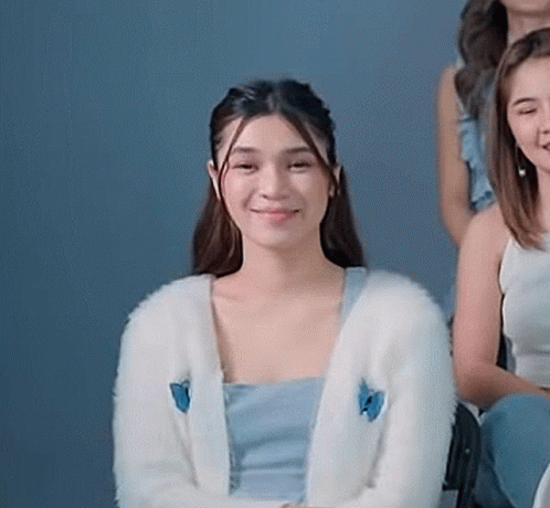 A Woman Wearing A White Cardigan With A Blue Butterfly On It Is Sitting Next To A Group Of Women . GIF