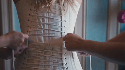 A Woman Wearing A White Corset Is Being Laced Up GIF