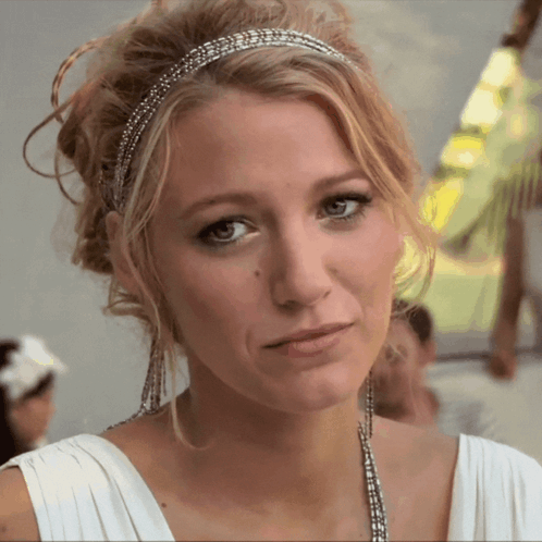A Woman Wearing A White Dress And A Headband Looks At The Camera GIF