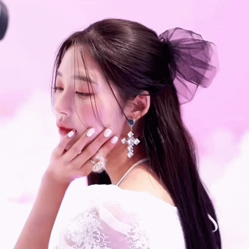 A Woman Wearing A White Dress And Earrings Has Her Hand On Her Chin GIF