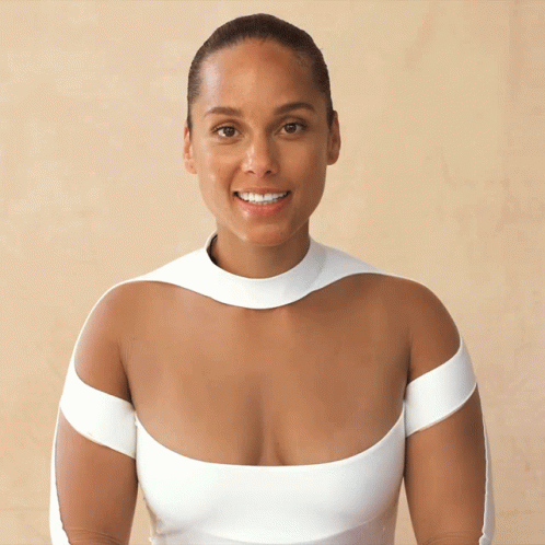 A Woman Wearing A White Dress With A Very Plunging Neckline Smiles For The Camera GIF