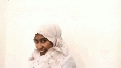 A Woman Wearing A White Hijab And A White Dress Is Smiling . GIF