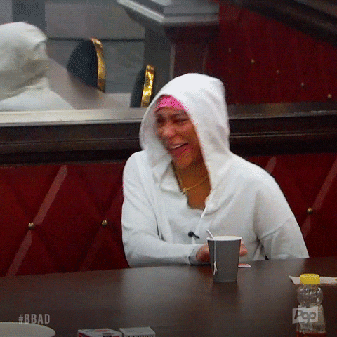 A Woman Wearing A White Hoodie Is Sitting At A Table With A Cup Of Coffee GIF