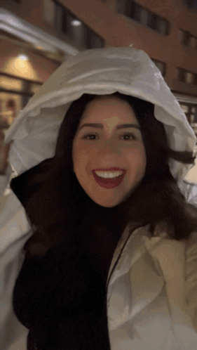 A Woman Wearing A White Jacket With A White Hood Is Smiling GIF