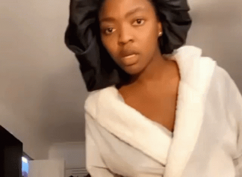 A Woman Wearing A White Robe And A Black Hat Is Making A Funny Face . GIF