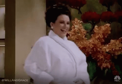 Woman In White Robe Standing In Front Of Flowers GIF