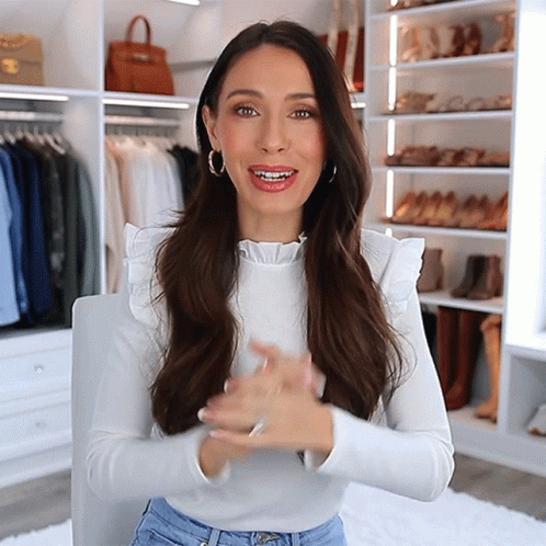 A Woman Wearing A White Ruffled Top Is Sitting In Front Of A Closet Full Of Clothes GIF