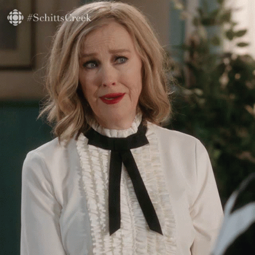 A Woman Wearing A White Shirt And A Black Bow Tie With #Schitts Creek On The Bottom GIF