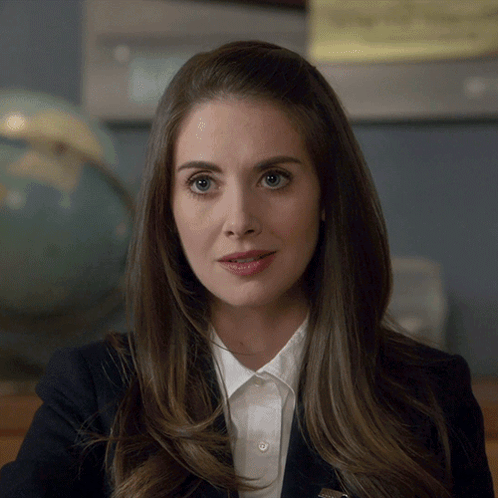 A Woman Wearing A White Shirt And A Black Jacket Has A Pin On Her Collar GIF